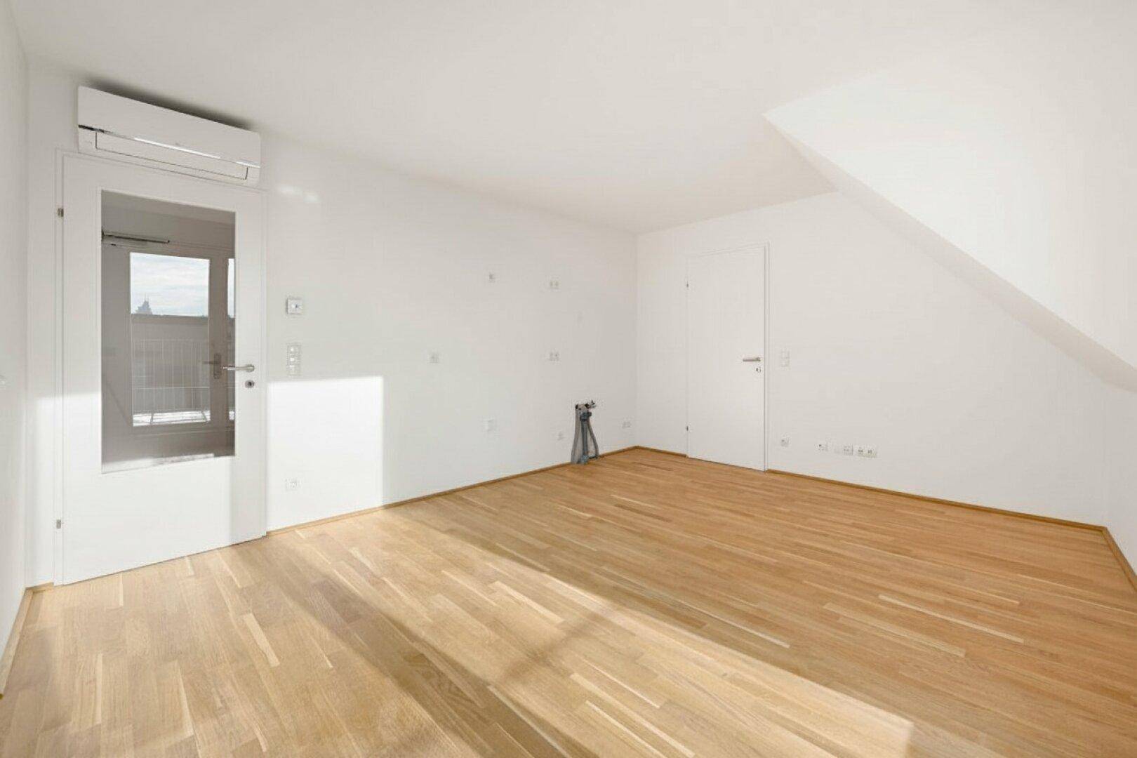 Heller Raum mit Holzboden, Klimaanlage und Zugang zu einem Außenbereich unter Dachschräge.