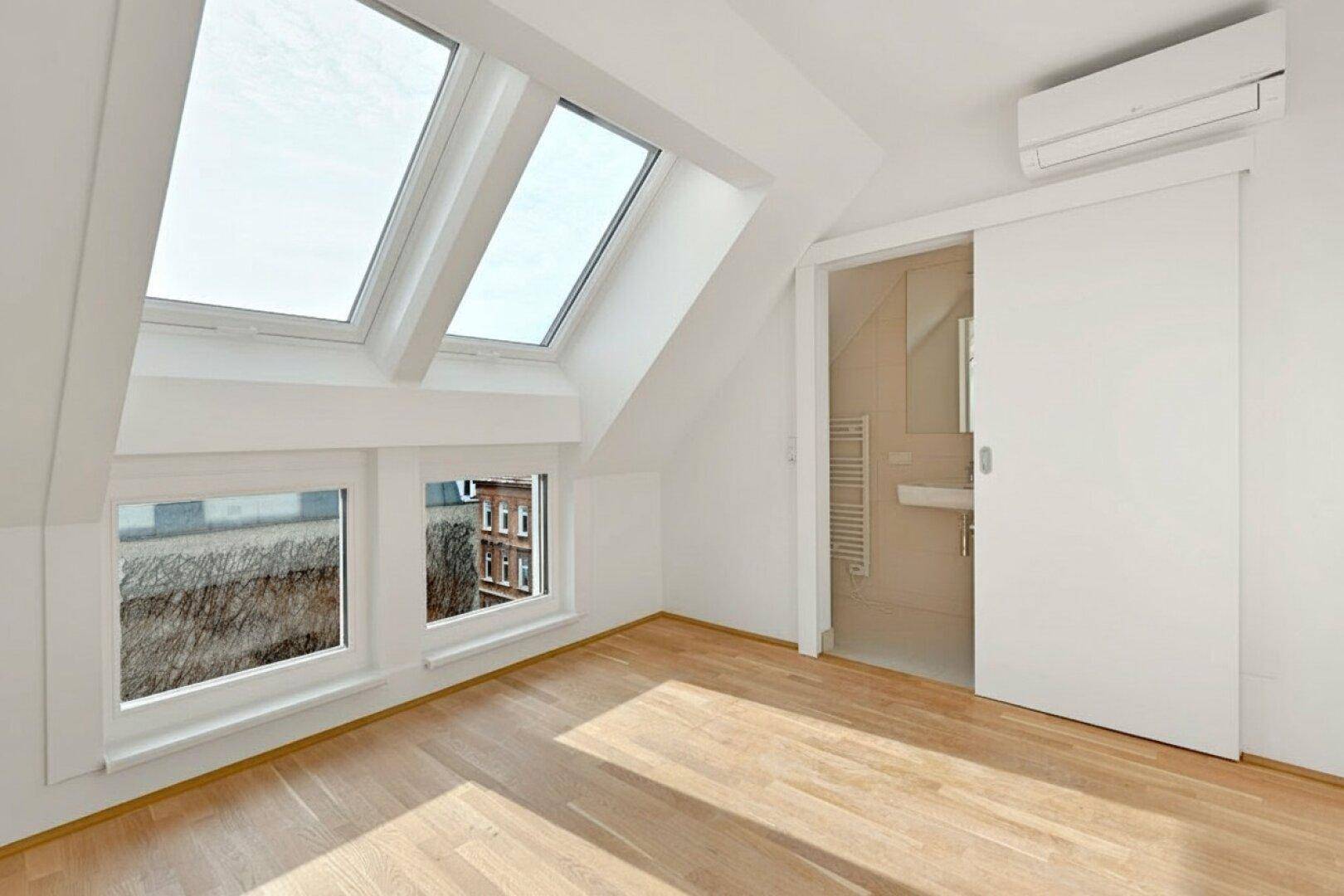 Lichtdurchfluteter Raum mit Holzboden, Dachfenstern und Schiebetür zum Badezimmer.