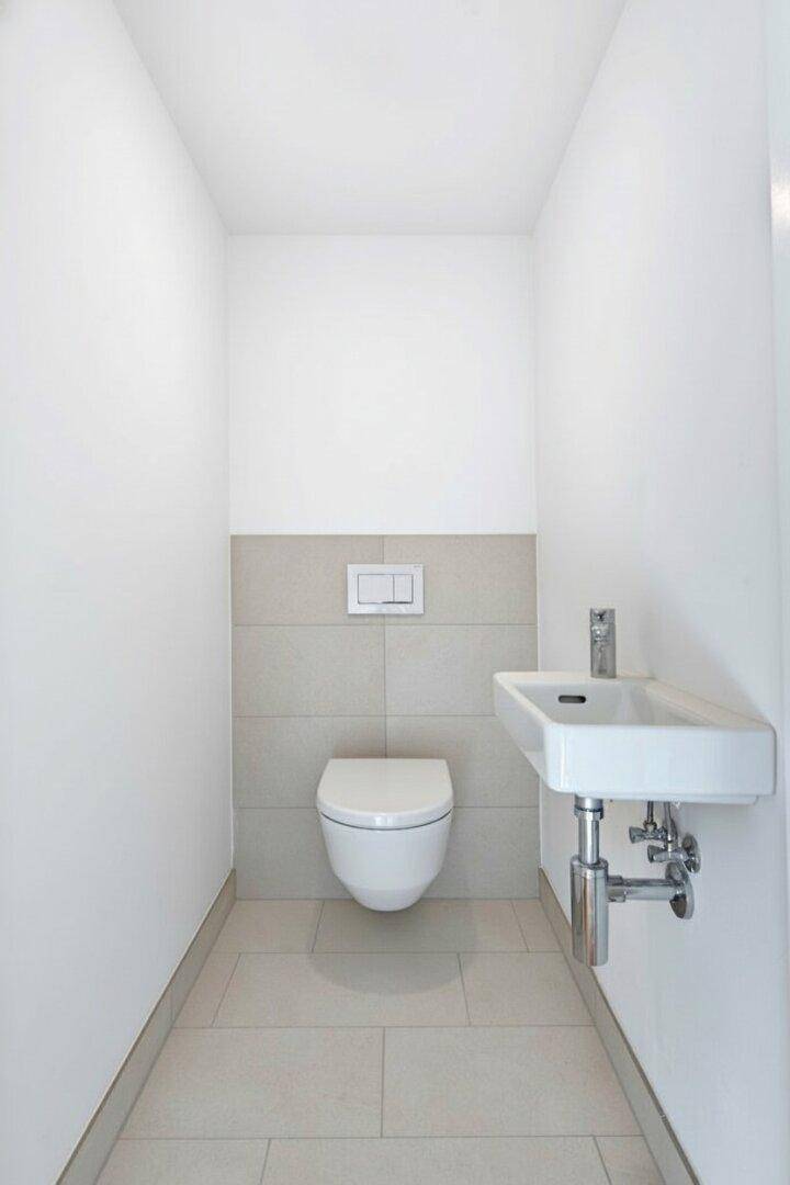 Modernes Gäste-WC mit wandhängender Toilette, kleinem Waschbecken und hellen Fliesen.
