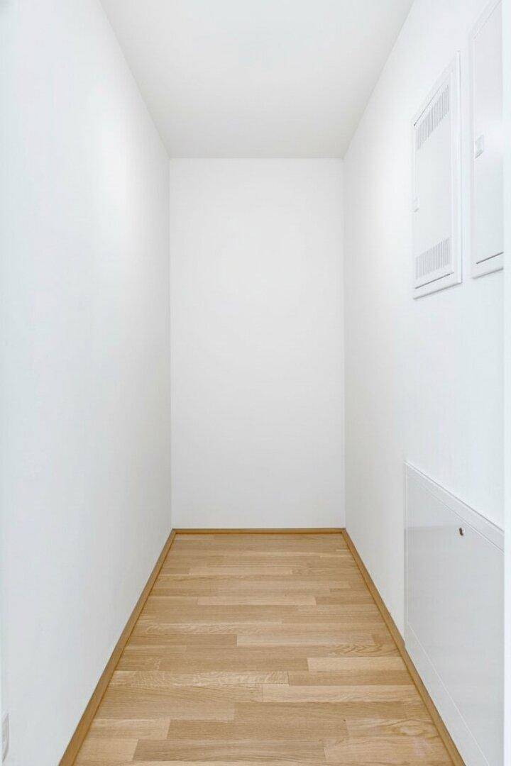 Schmaler Abstellraum oder Flur mit Holzboden und weißen Wänden, ideal für Lagerung.