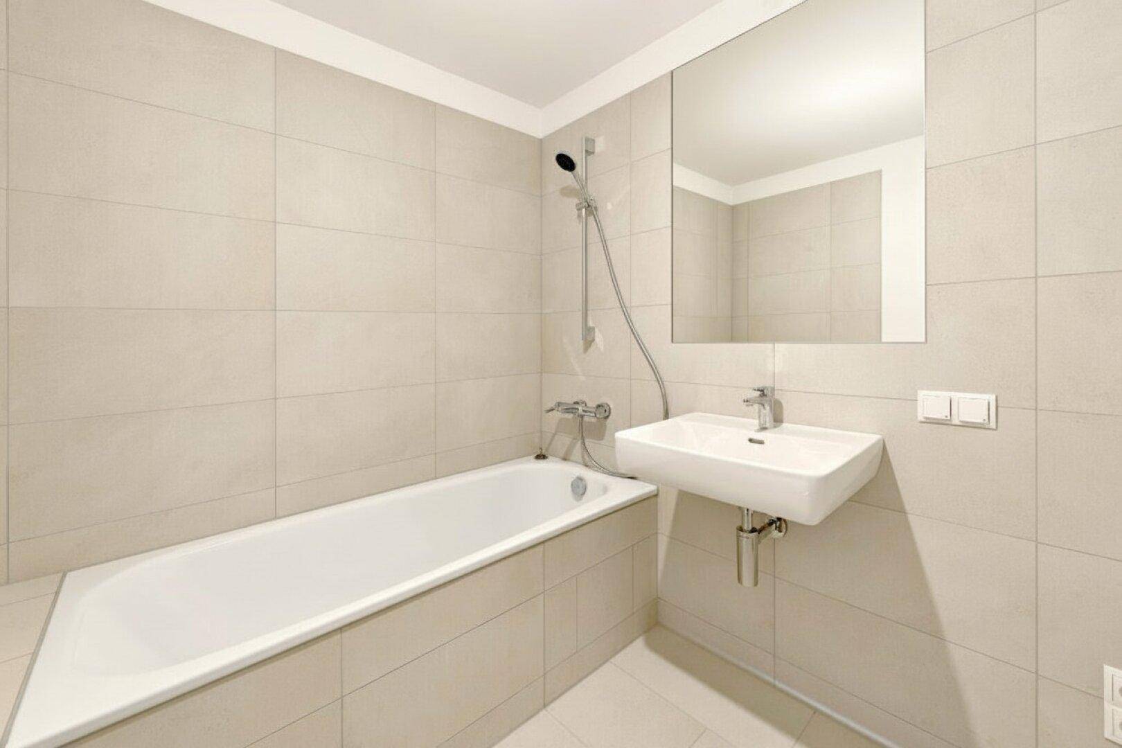 Modernes Badezimmer mit Badewanne, Einzelwaschbecken und hellen Fliesen an den Wänden.