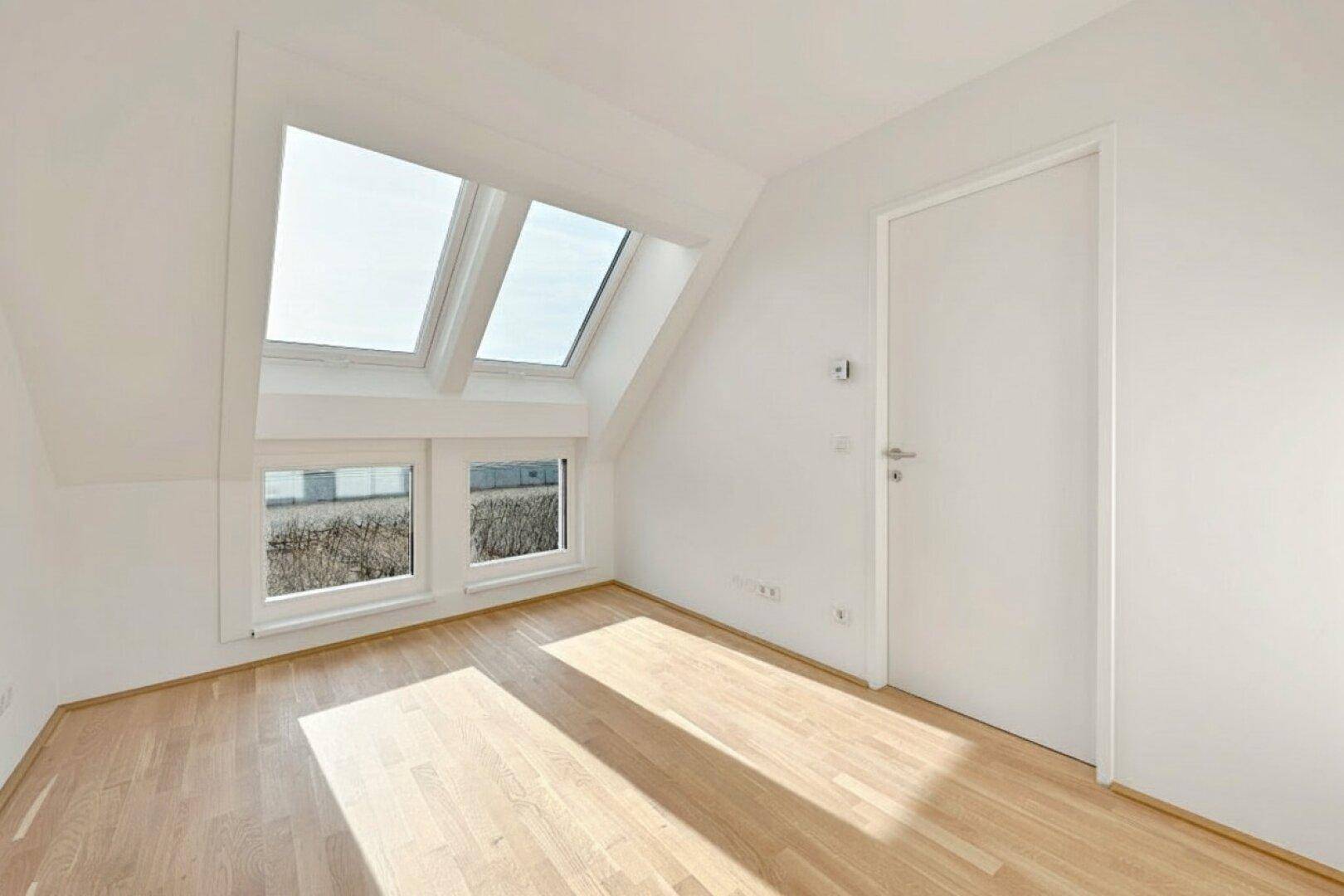 Lichtdurchfluteter Raum mit Holzboden, mehreren Dachfenstern und weiß gestrichenen Wänden.