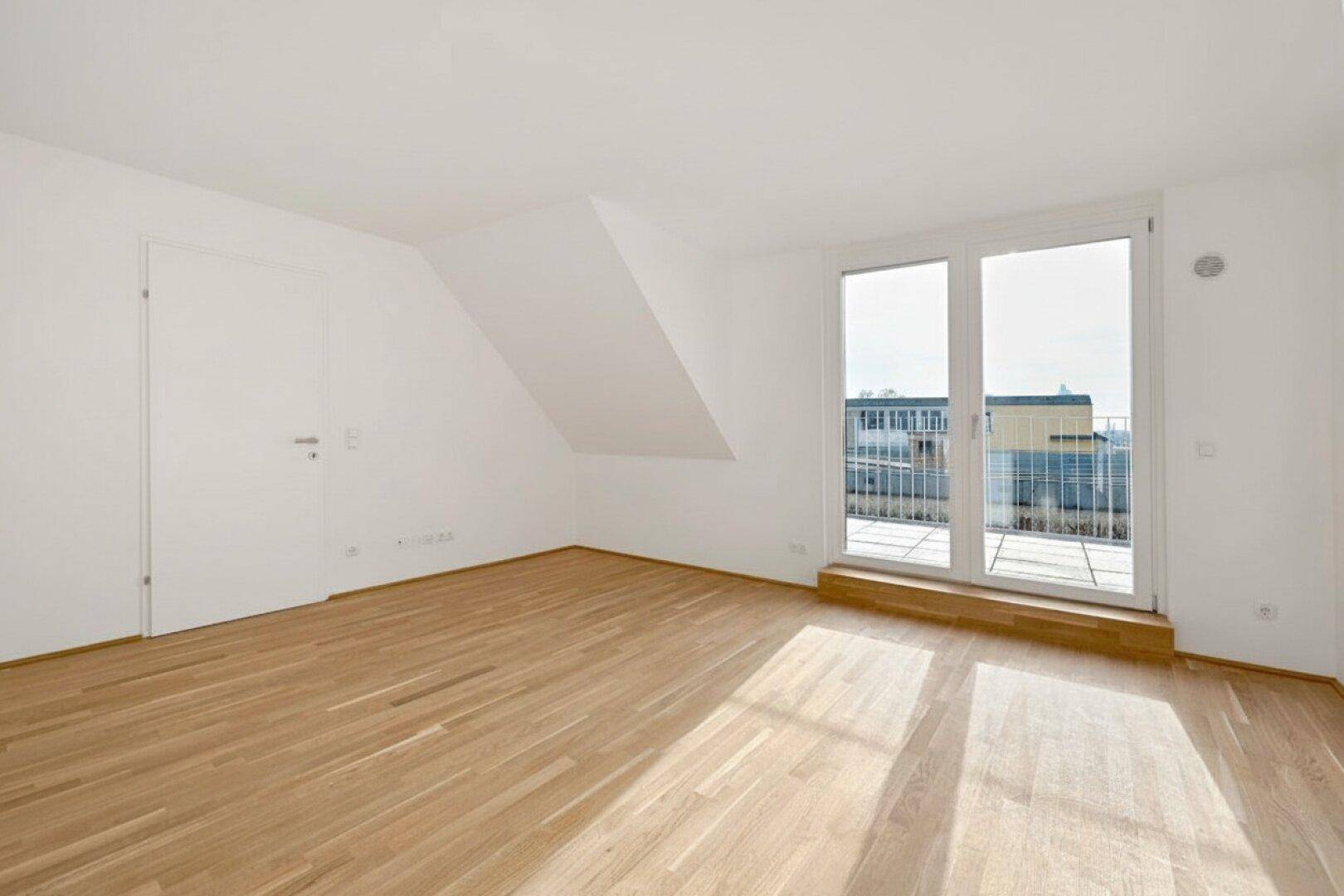 Geräumiger, leerer Raum mit Holzboden und großem Fenster mit Zugang zu einer Terrasse.