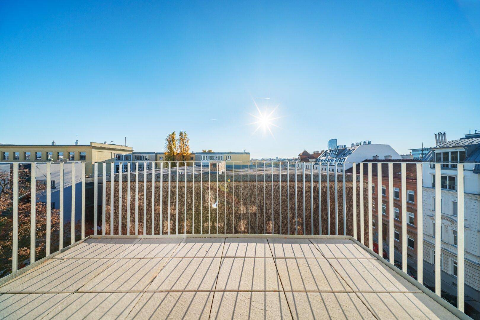 Sonnige Dachterrasse mit weitem Blick über die Stadt und umliegende Gebäude.