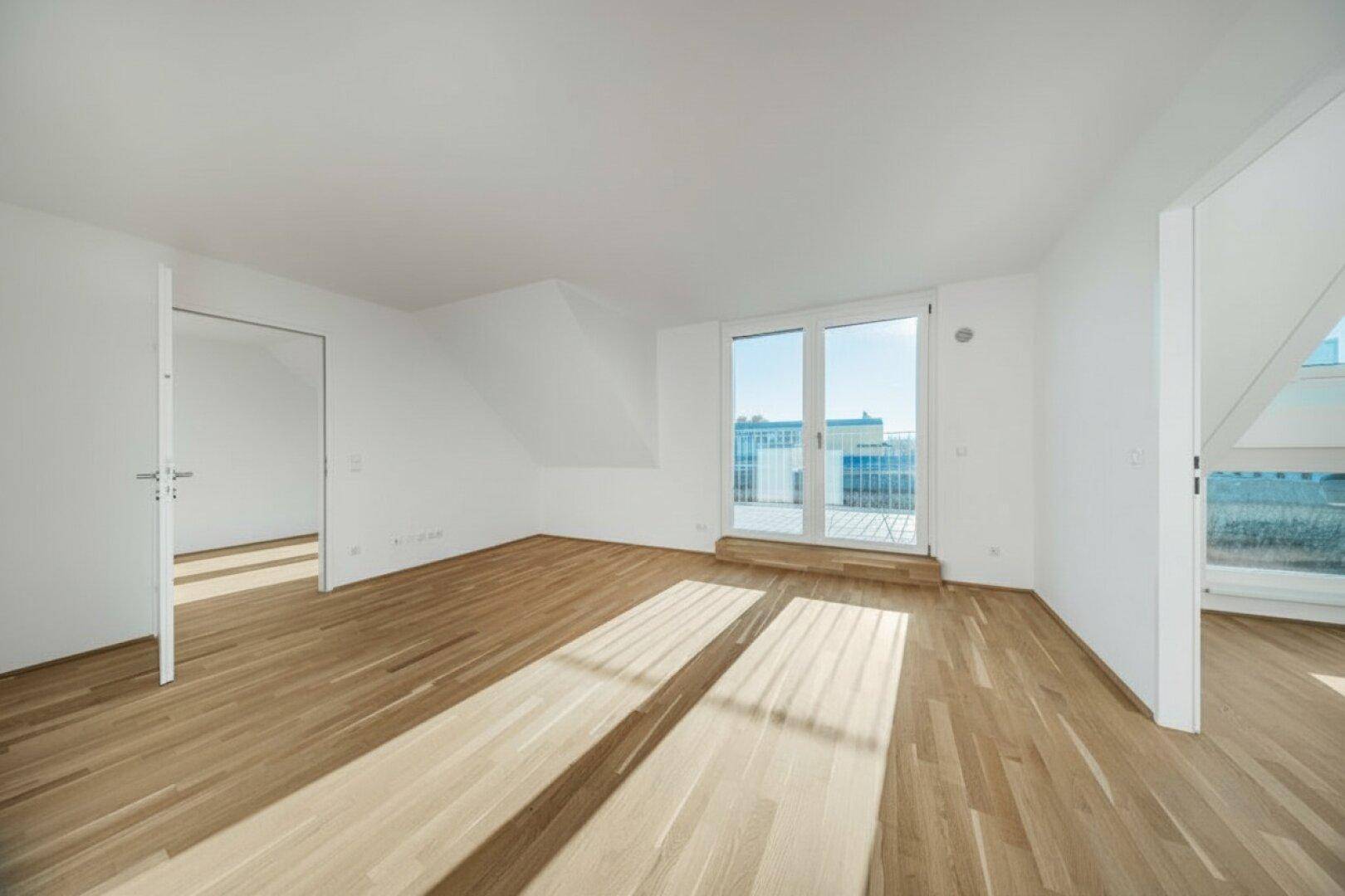 Heller, leerer Raum mit Holzboden und großen Fenstern, die Zugang zu einer Terrasse bieten.