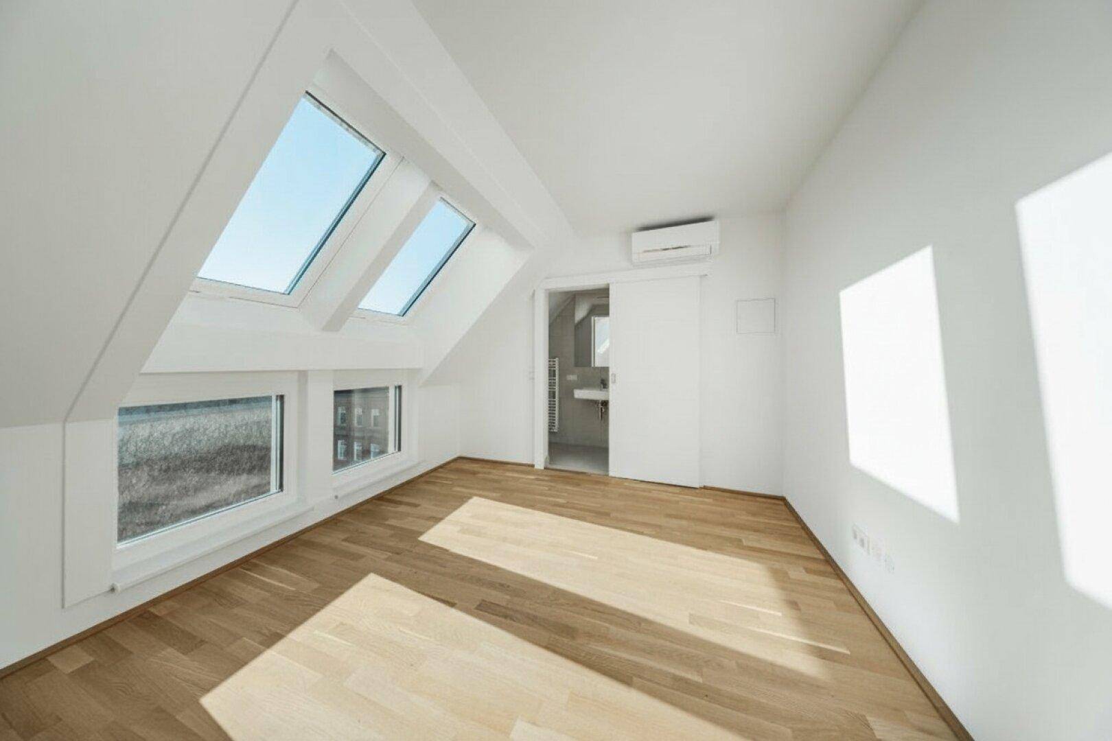 Helles Zimmer im Dachgeschoss mit Holzboden, Dachfenstern und Klimaanlage für Komfort.