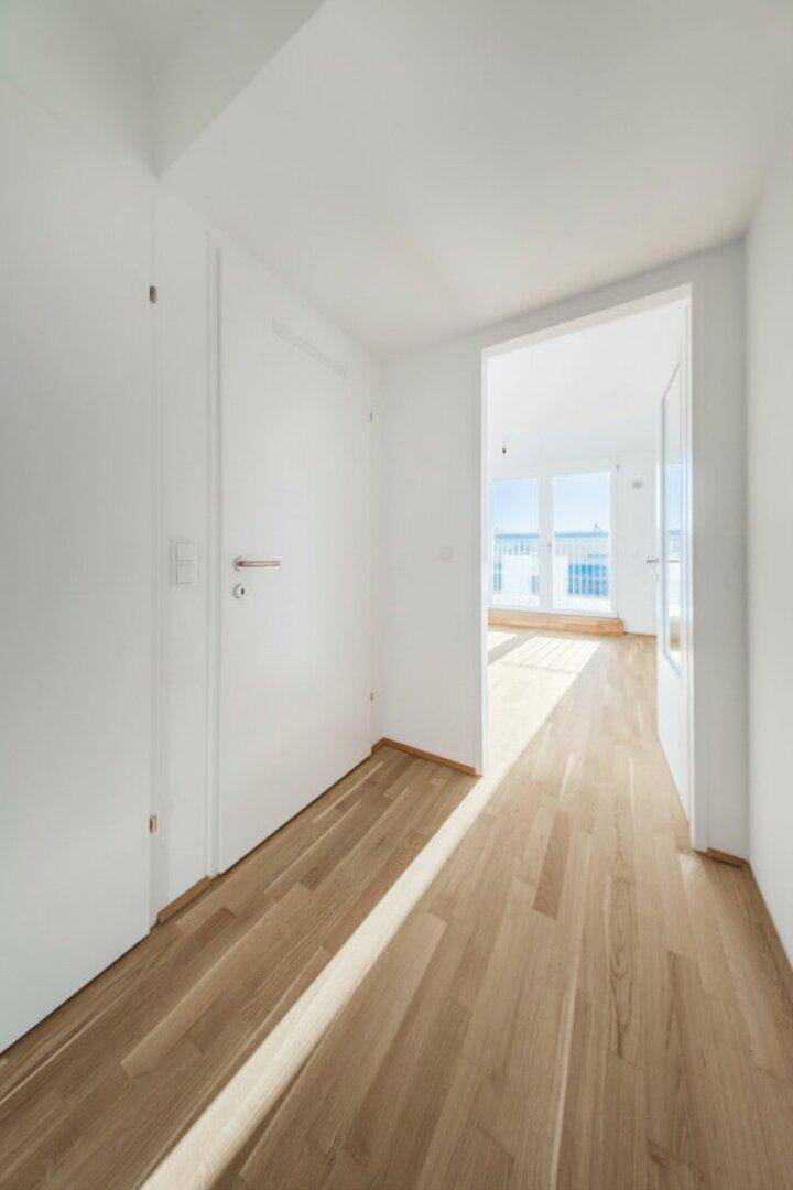 Heller Flur mit Holzboden, der zu weiteren Räumen und einem lichtdurchfluteten Bereich führt.
