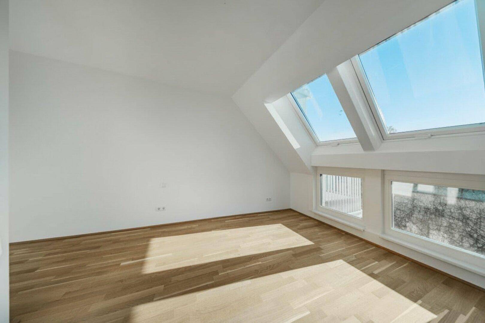 Dachgeschosszimmer mit Holzboden und mehreren Dachfenstern, die viel Tageslicht hereinlassen.