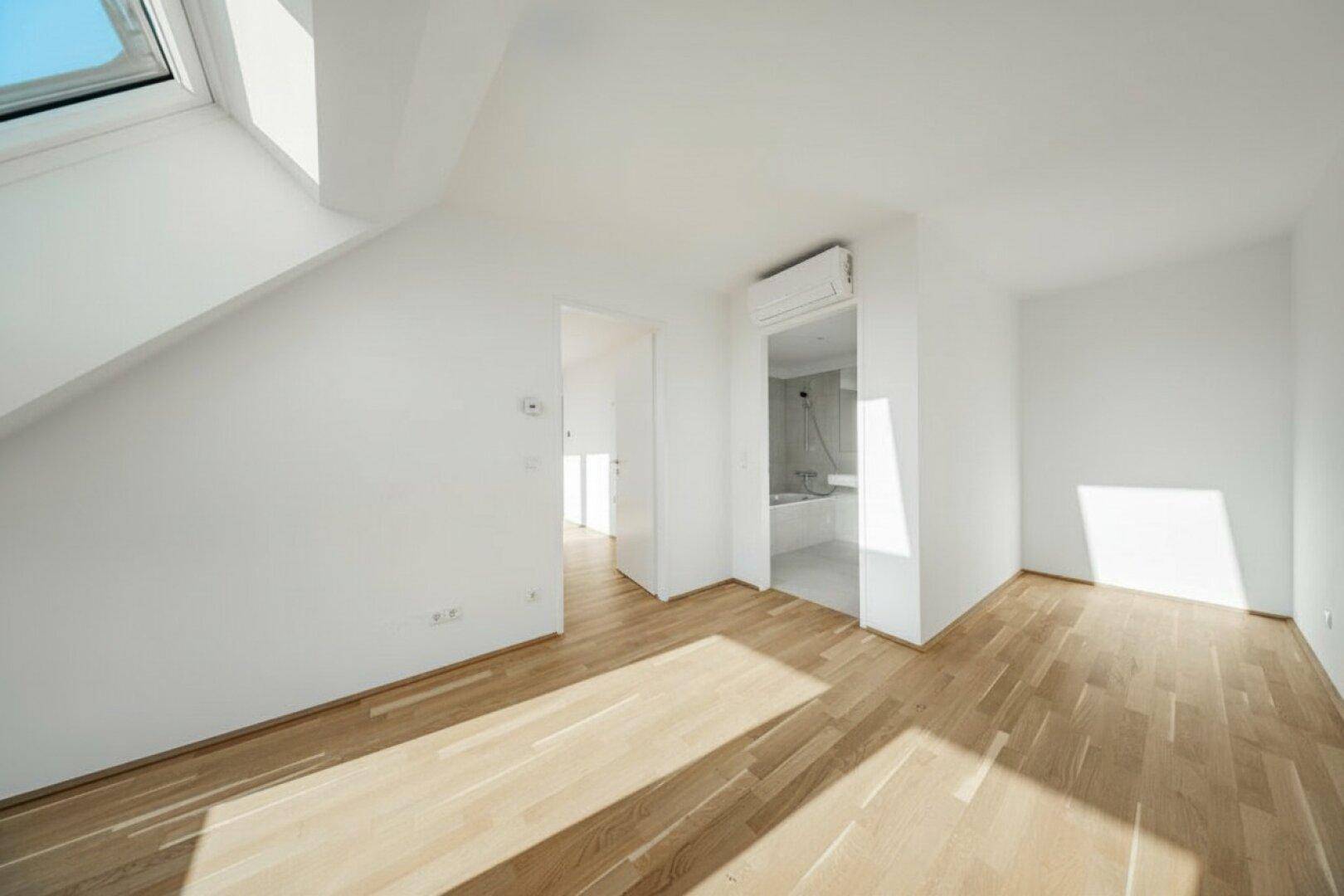 Helles Zimmer mit Holzboden, Klimaanlage und direktem Zugang zu einem modernen Badezimmer.
