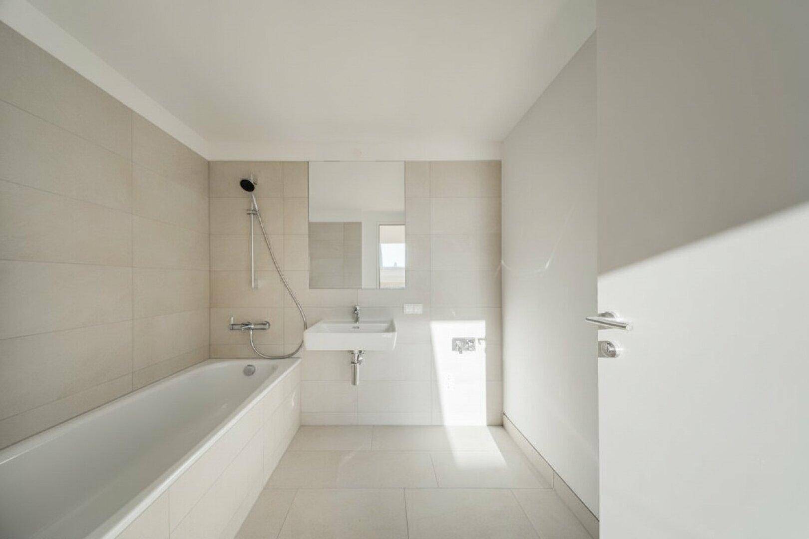 Modernes Badezimmer mit Badewanne, Wandwaschbecken und hellen Fliesen an Wänden und Boden.