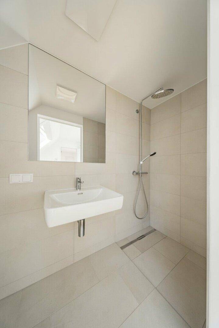 Zeitgemäßes Badezimmer mit ebenerdiger Dusche, Wandwaschbecken und großformatigen Fliesen.