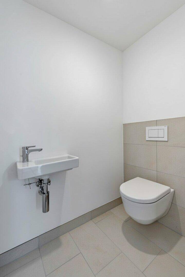 Modernes Gäste-WC mit wandhängender Toilette, kleinem Waschbecken und hellen Fliesen.