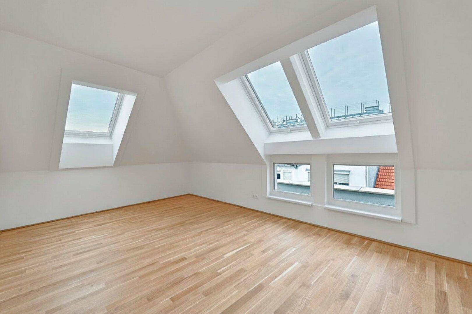 Geräumiges Zimmer im Dachgeschoss mit Holzboden, schrägen Wänden und mehreren Dachfenstern.