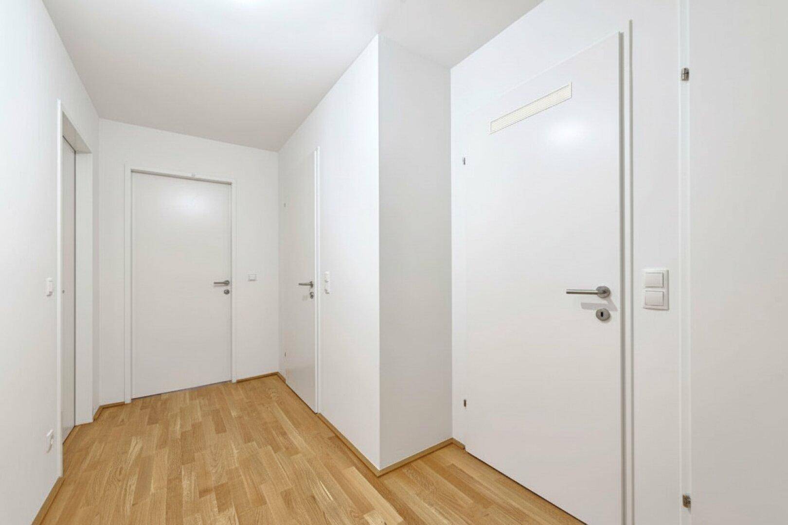 Heller Flur mit Holzboden und mehreren weißen Türen, der zu verschiedenen Räumen führt.