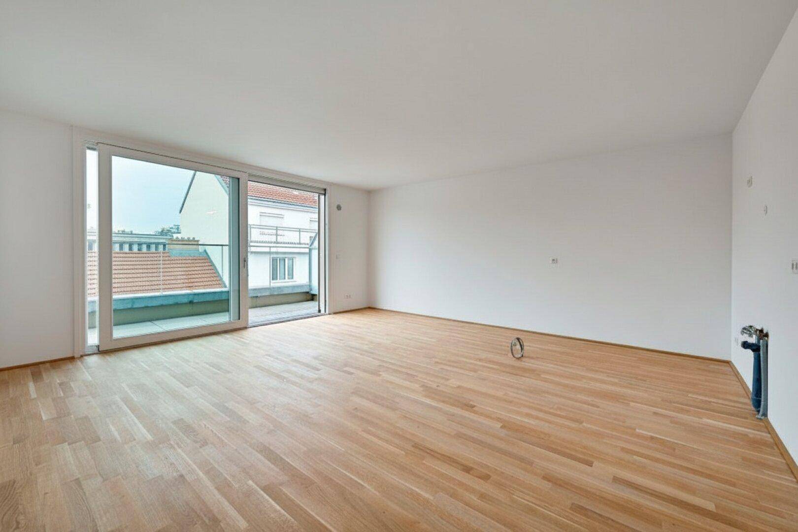 Geräumiger leerer Raum mit Holzboden und großem Schiebefenster zum Balkon.