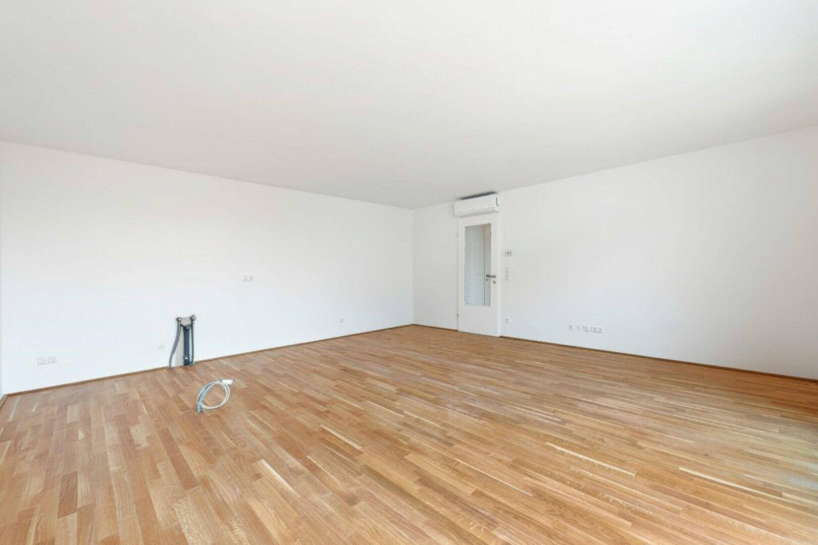 Geräumiger leerer Raum mit Holzboden, Klimaanlage und Vorinstallationen für eine Küche.