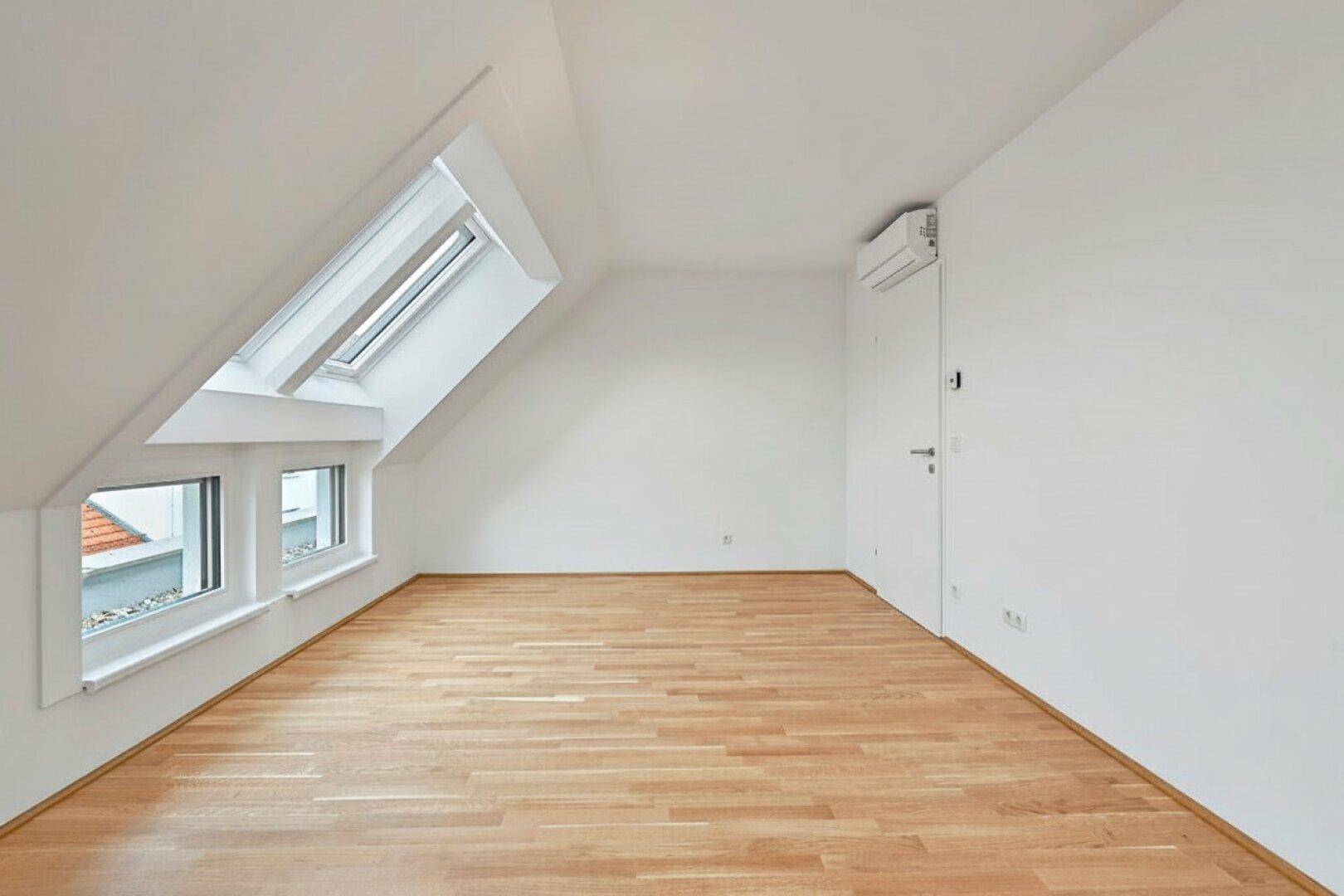Helles Zimmer im Dachgeschoss mit Holzboden, Klimaanlage und einem großen Dachfenster.