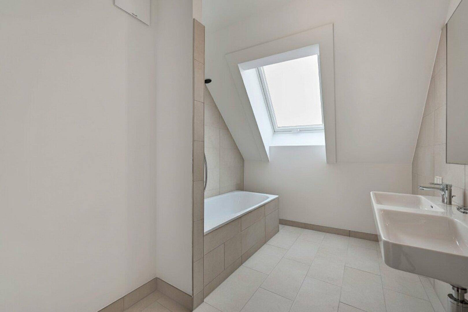 Helles Badezimmer im Dachgeschoss mit Badewanne, Doppelwaschbecken und Dachfenster.