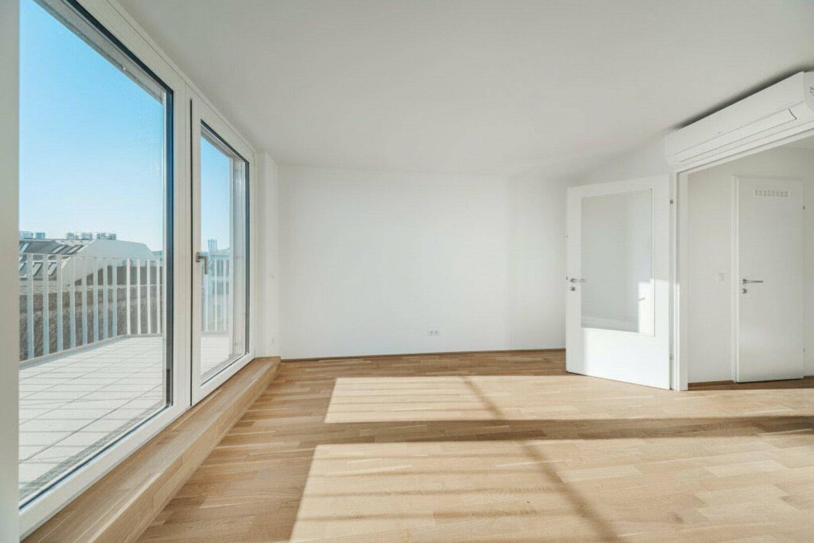 Heller Wohnraum mit großen Fenstern, Holzboden und Zugang zu einem Balkon.