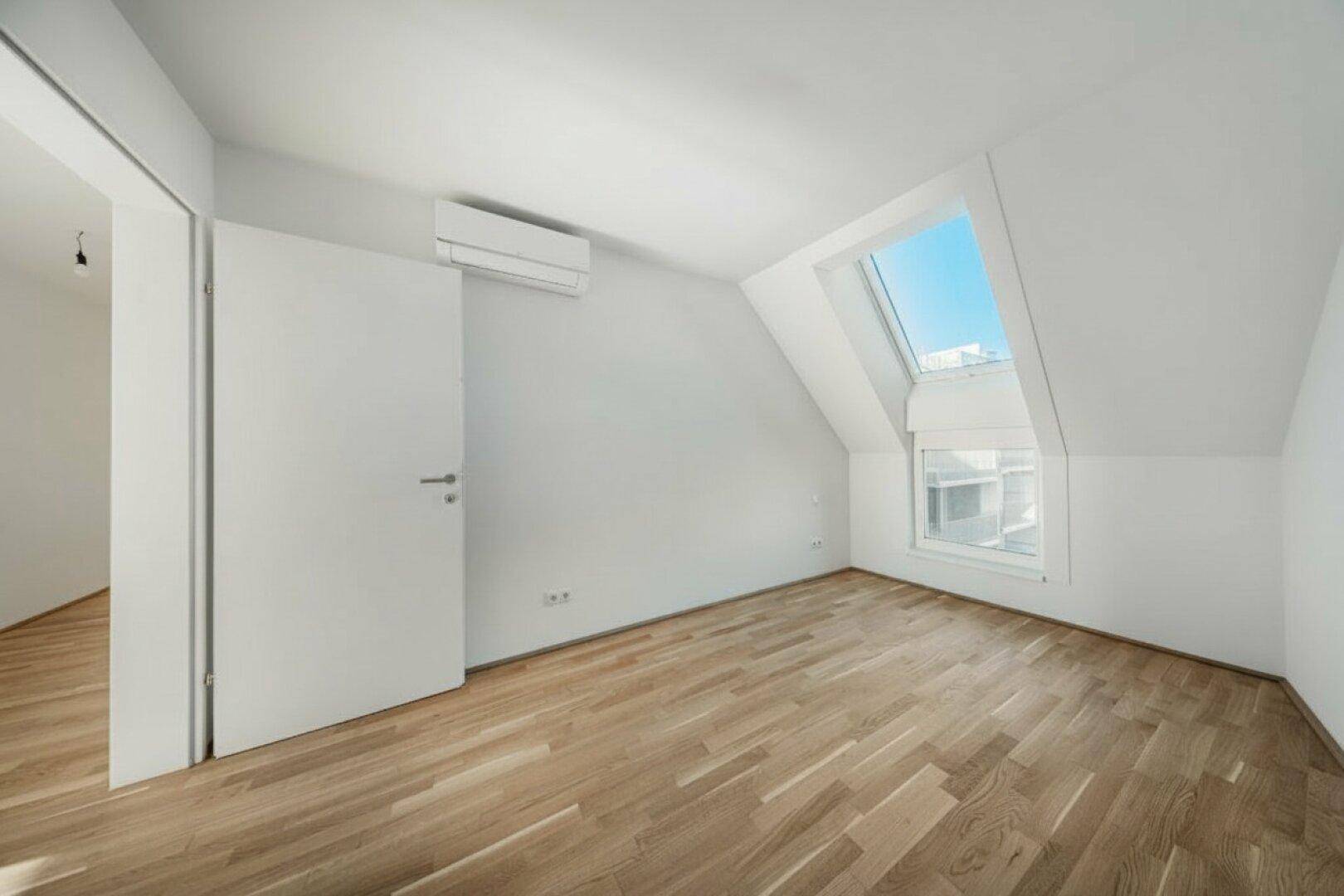 Helles Schlafzimmer im Dachgeschoss mit Holzboden, Dachschräge und Dachfenster.
