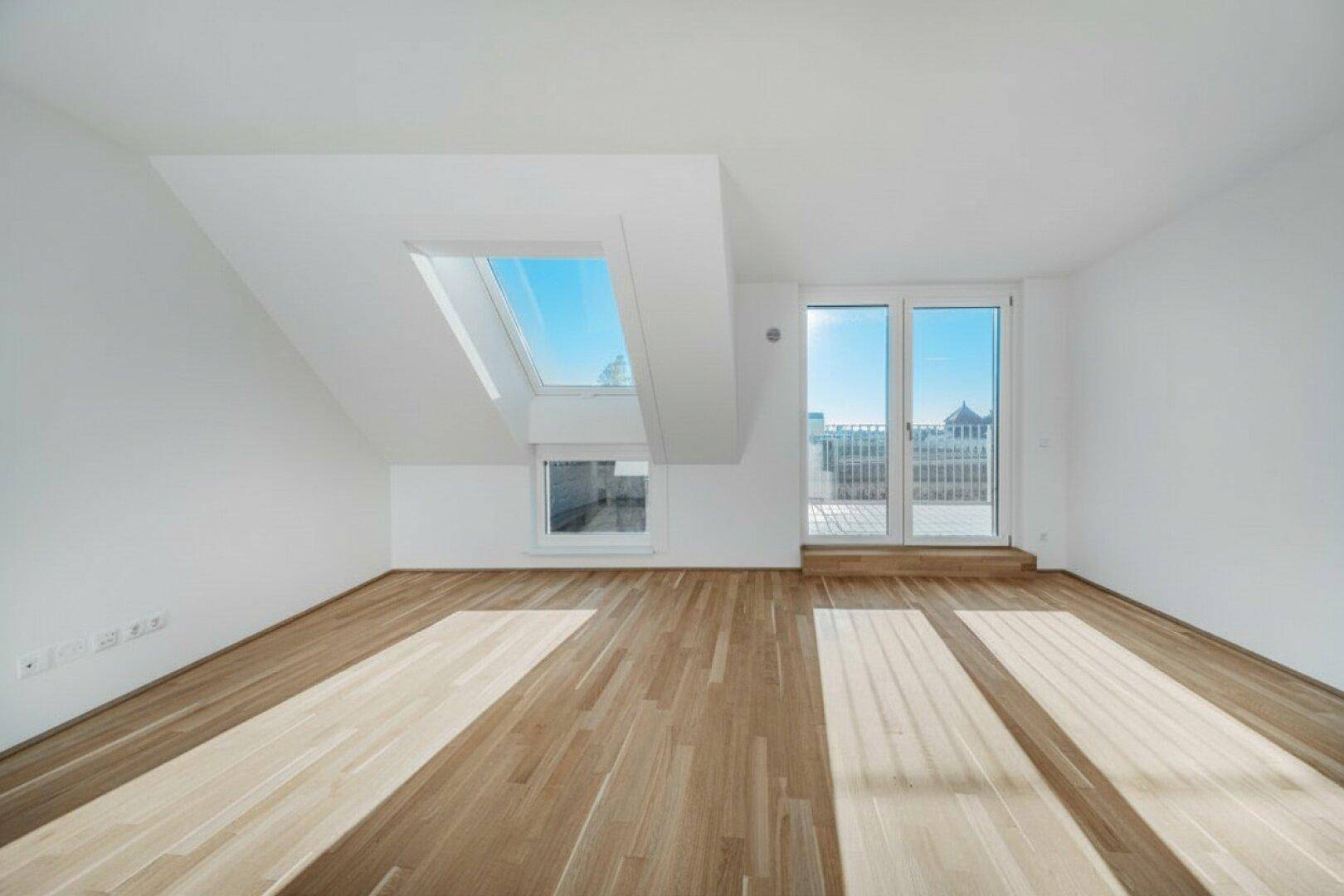 Geräumiger Wohnraum mit Holzboden, Dachfenstern und Zugang zu einem Balkon.