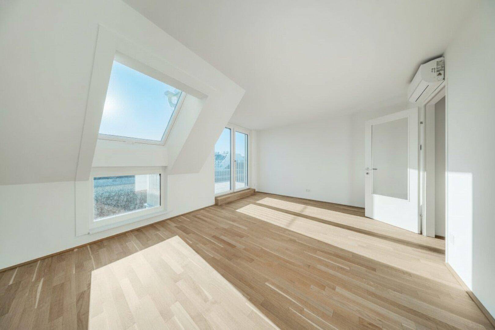 Heller Wohnraum mit Holzboden, Dachfenstern und Zugang zu einem Balkon.