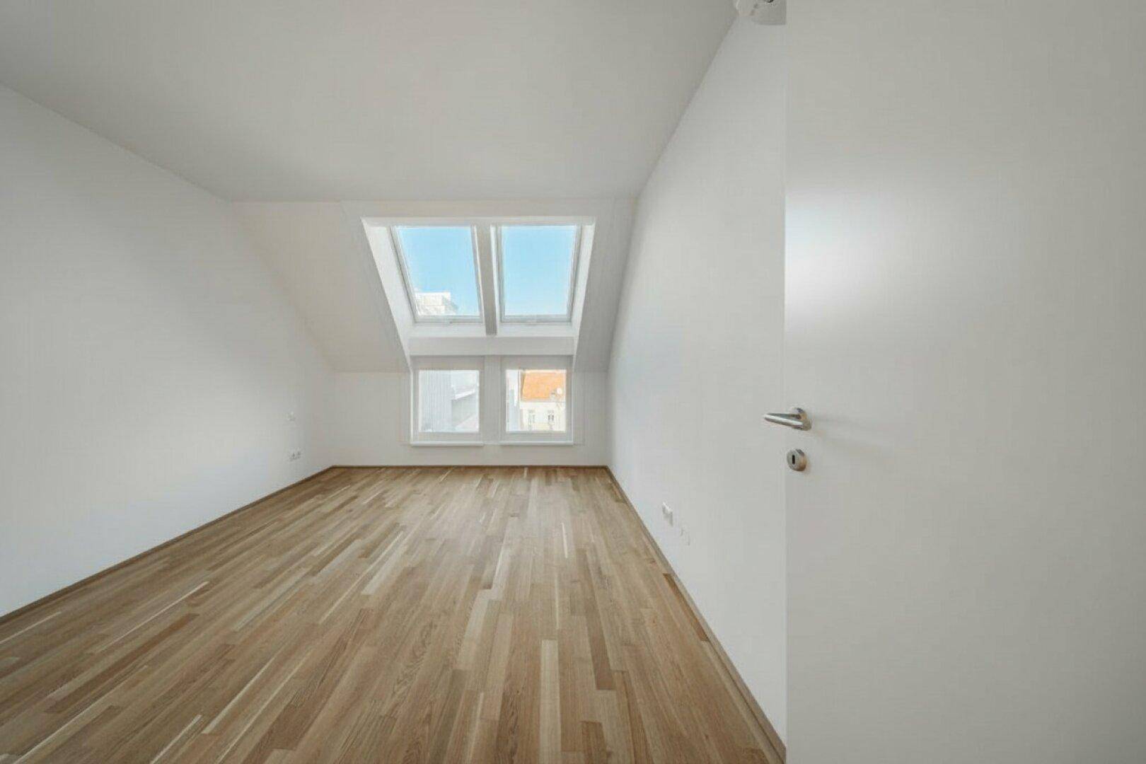 Helles Schlafzimmer im Dachgeschoss mit Holzboden, Dachschräge und Dachfenstern.