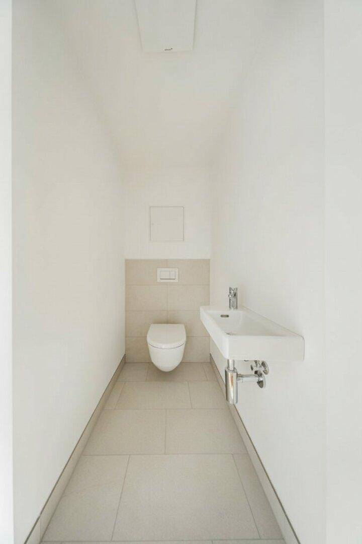 Modernes Gäste-WC mit Wand-WC, Waschbecken und hellen Fliesen.