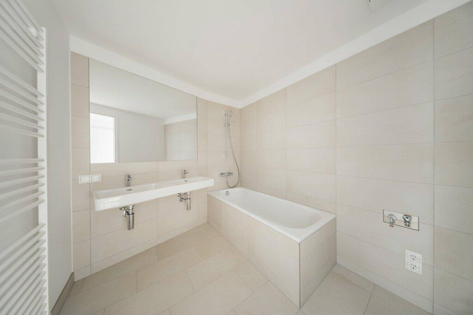 Modernes Badezimmer mit Doppelwaschbecken, Badewanne und hellen Fliesen.