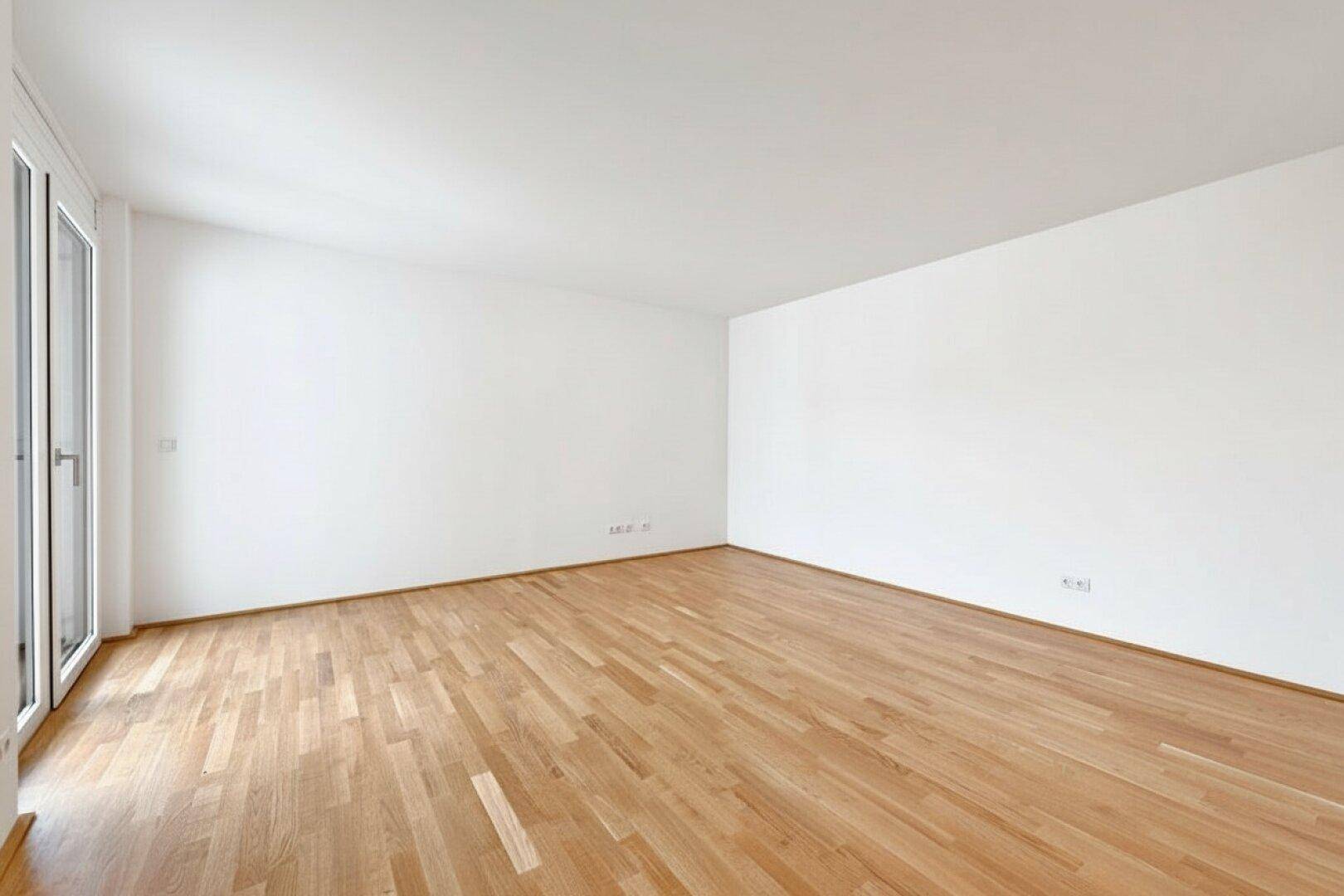 Heller, leerer Raum mit Eichenparkettboden und Zugang zu einem Balkon oder einer Terrasse.