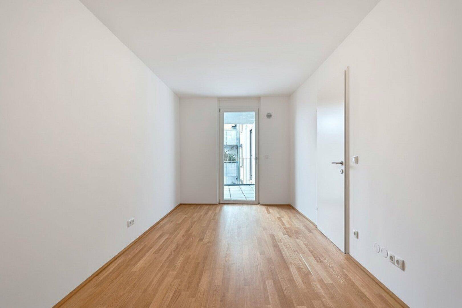 Heller, leerer Raum mit Parkettboden und Zugang zu einem französischen Balkon.