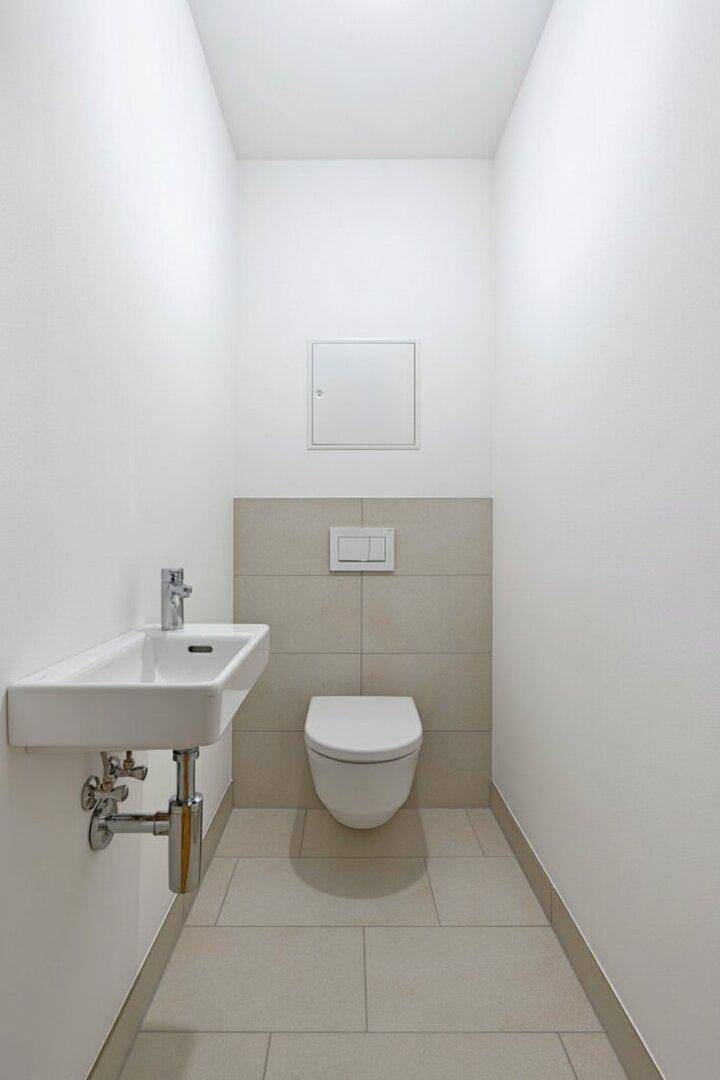 Modernes Gäste-WC mit wandhängender Toilette, kleinem Waschbecken und hellen Fliesen.