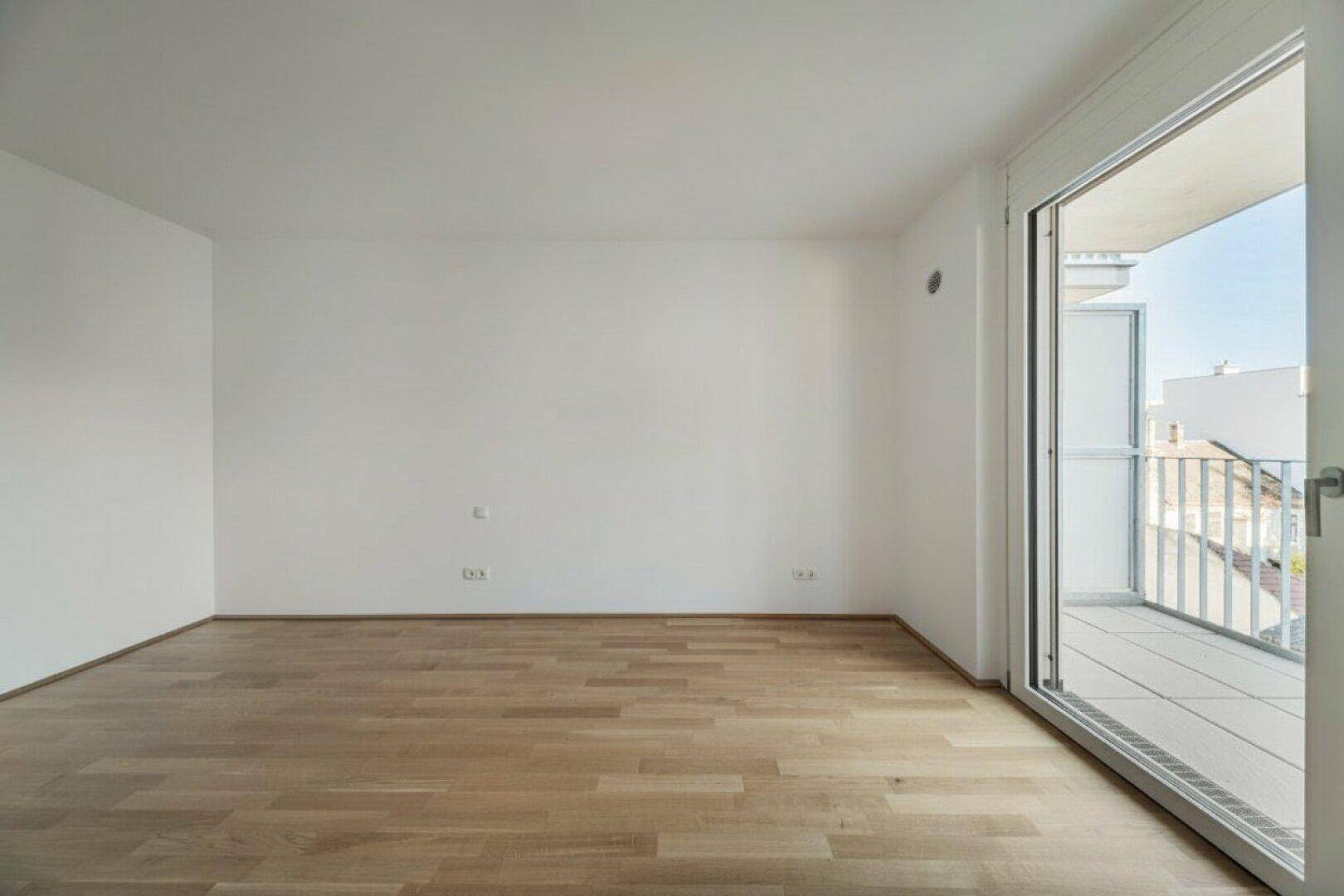 Leerer Raum mit Parkettboden und Zugang zu einem Balkon, ideal als Schlaf- oder Wohnzimmer.
