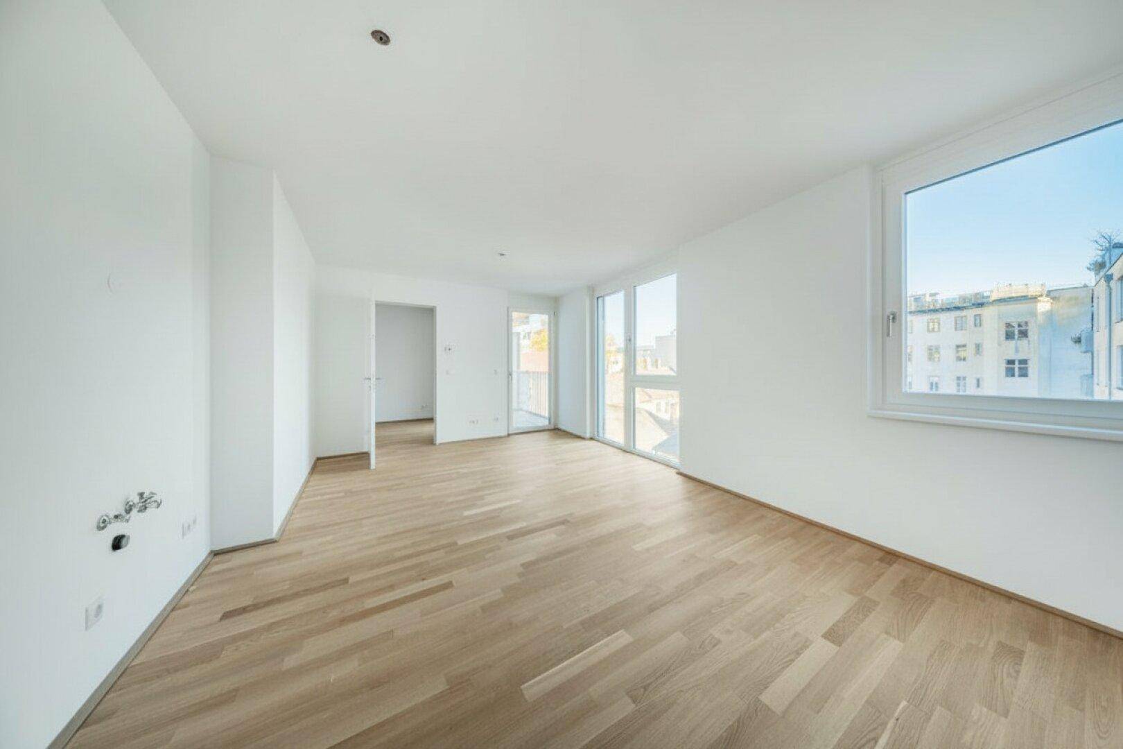 Helles, leeres Wohnzimmer mit großen Fenstern und Parkettboden, bereit zur individuellen Gestaltung.