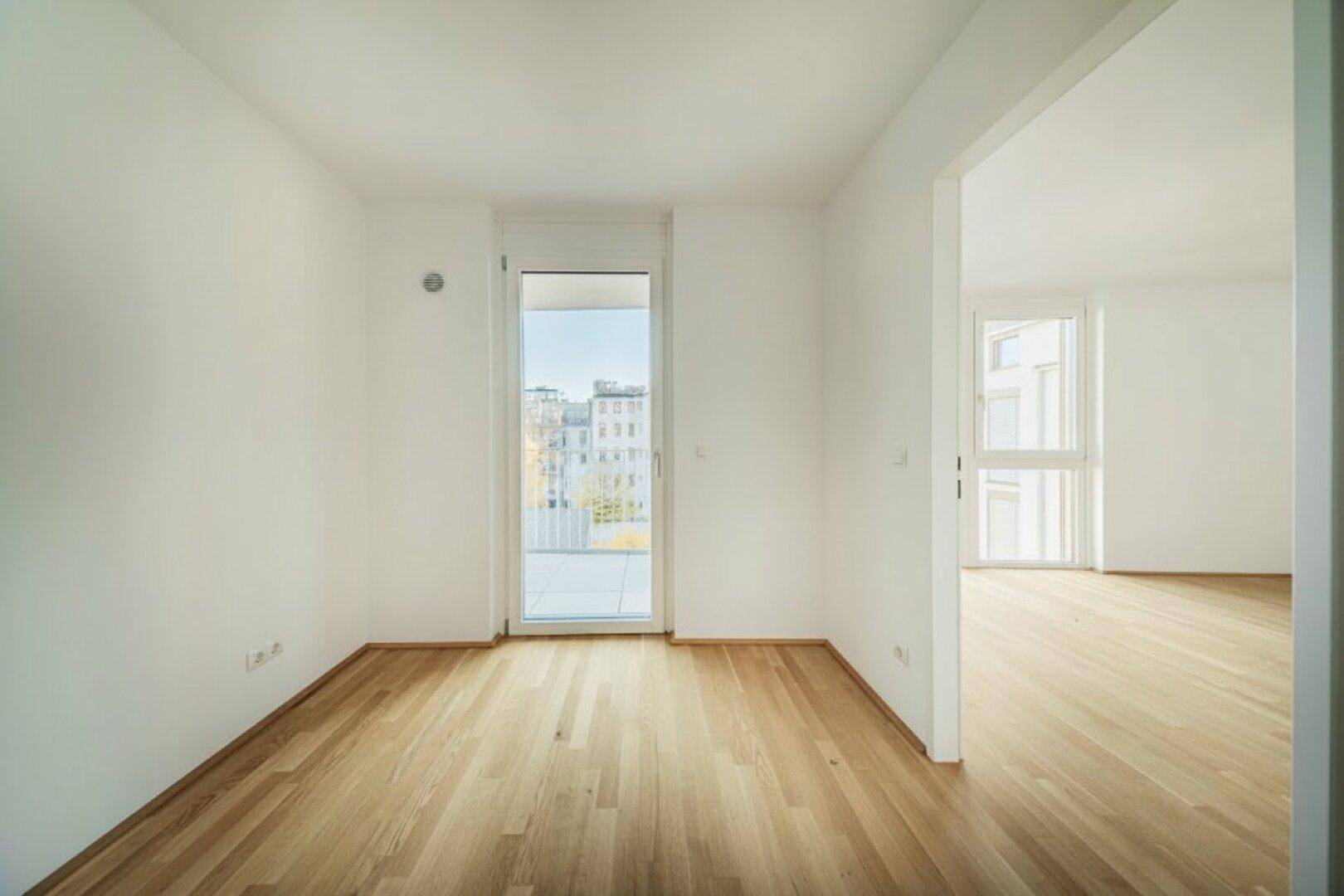 Heller Raum mit Parkettboden und Balkonzugang, geeignet als Schlaf- oder Arbeitszimmer.
