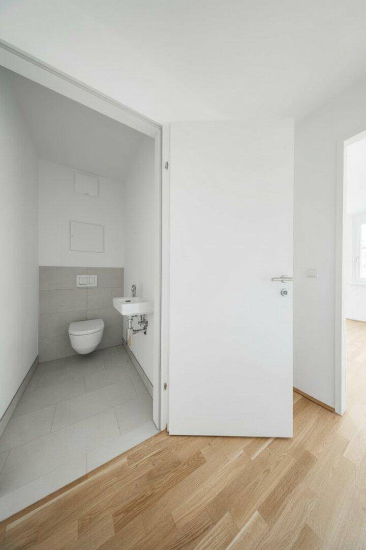 Separates Gäste-WC mit wandhängendem WC und kleinem Waschbecken, modern gefliest.