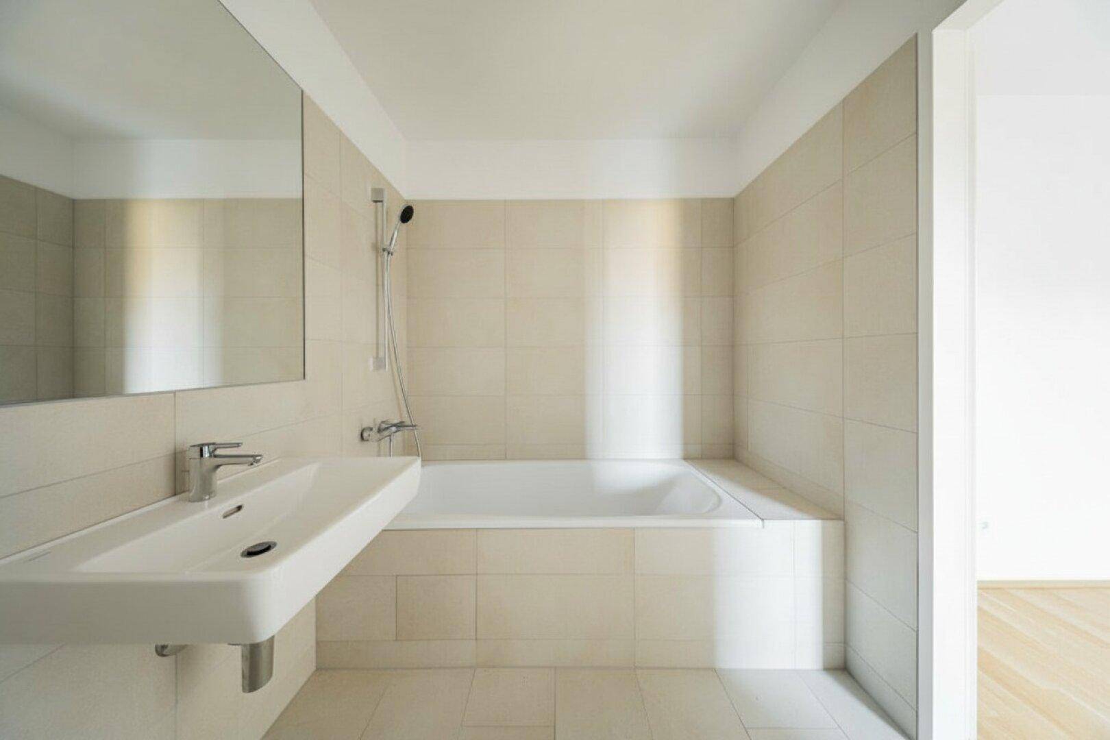 Modernes Badezimmer mit Badewanne, Waschbecken und hellen Fliesen, in neutralen Farbtönen gehalten.