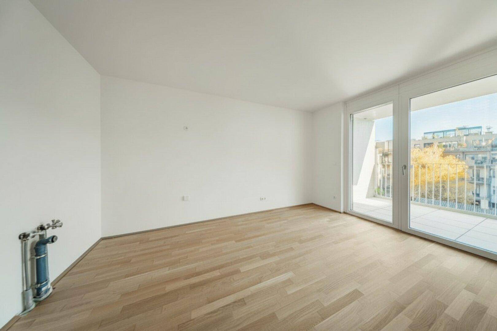 Helles, leeres Zimmer mit Holzboden und Balkonzugang, bereit zur individuellen Gestaltung.