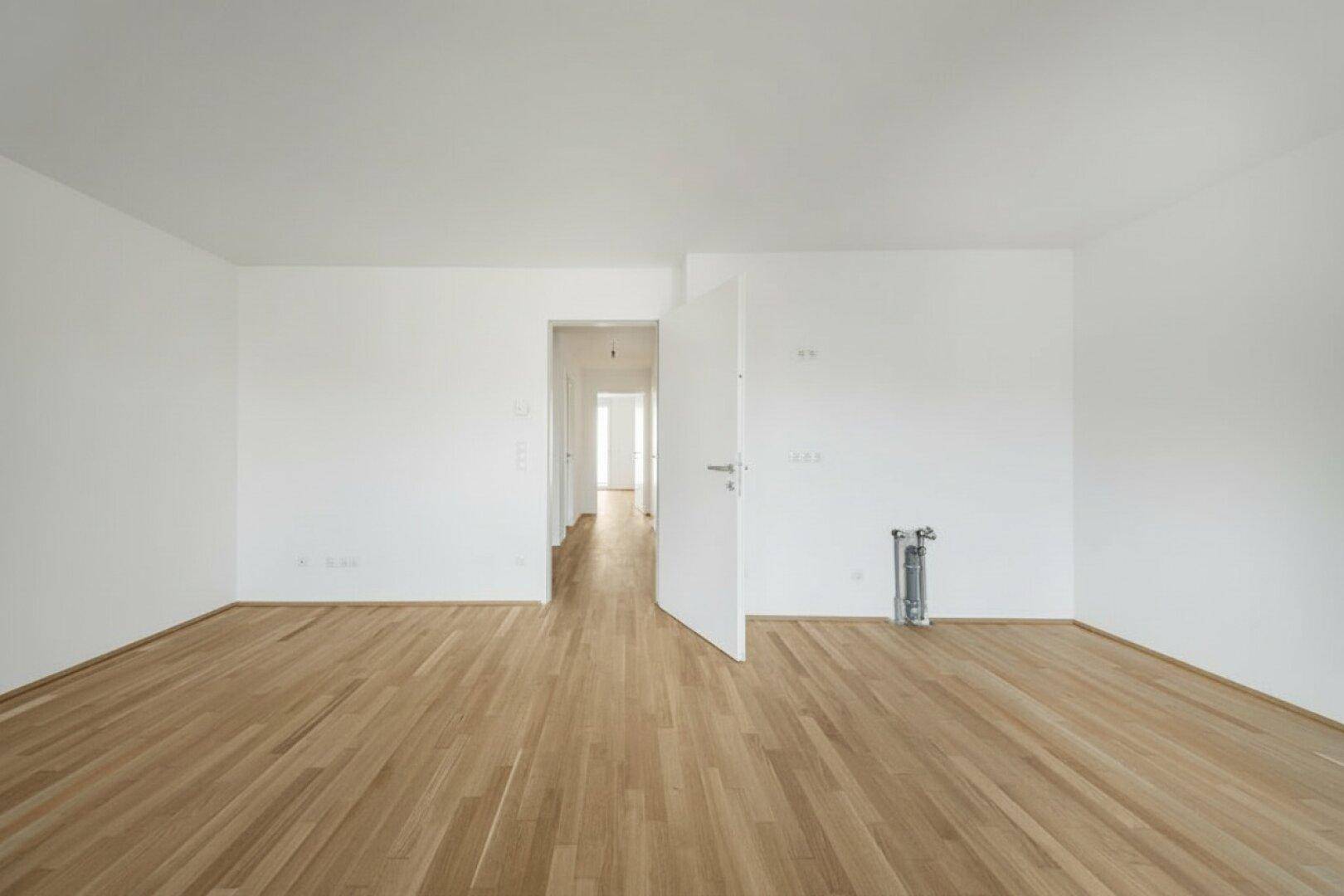 Leeres Zimmer mit Holzboden und offener Tür zu einem Flur, ideal für individuelle Einrichtung.