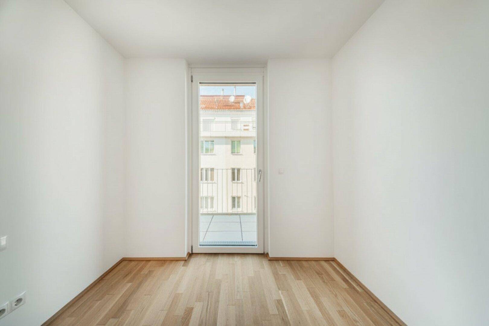 Helles, leeres Schlafzimmer mit Holzboden und französischem Balkon, ideal für ein Kinderzimmer.