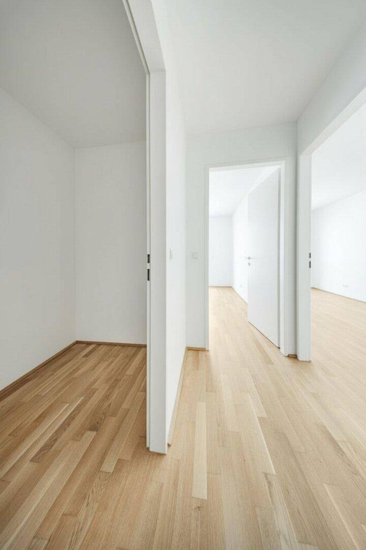 Heller Flur mit Holzboden und weißen Wänden, der zu verschiedenen Räumen führt.