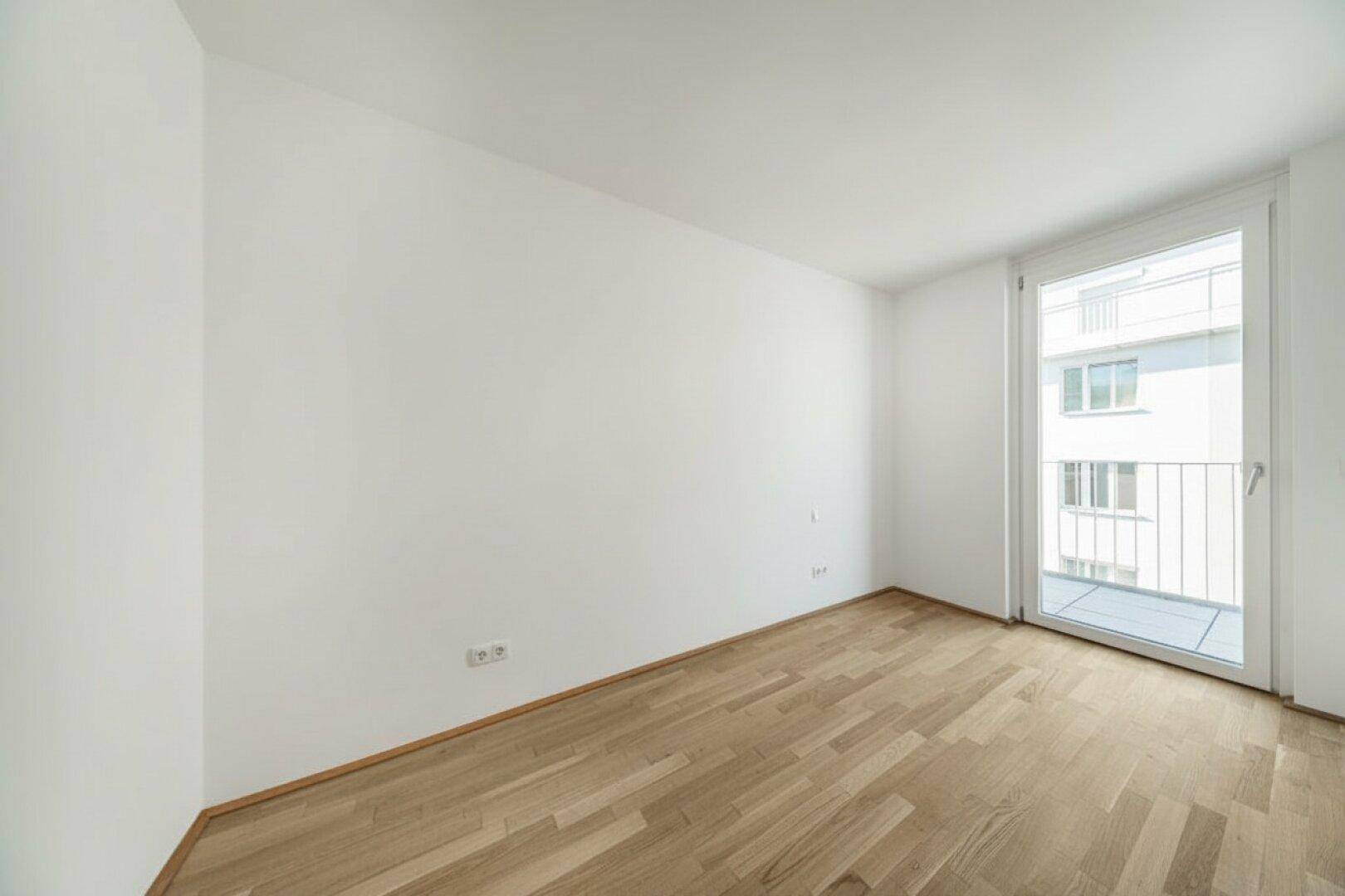 Leeres Schlafzimmer mit Holzboden und Balkonzugang, bereit für persönliche Gestaltung.