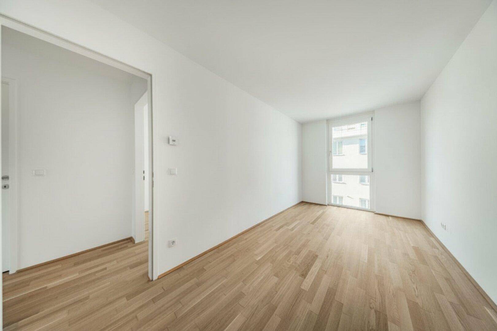 Helles, leeres Zimmer mit Holzboden und Fenster, ideal als Schlaf- oder Arbeitszimmer.