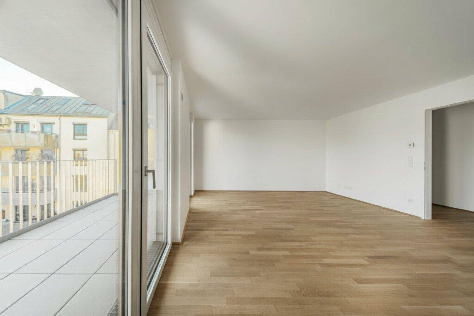 Weitläufiges, leeres Wohnzimmer mit Holzboden und großem Balkon, lichtdurchflutet.
