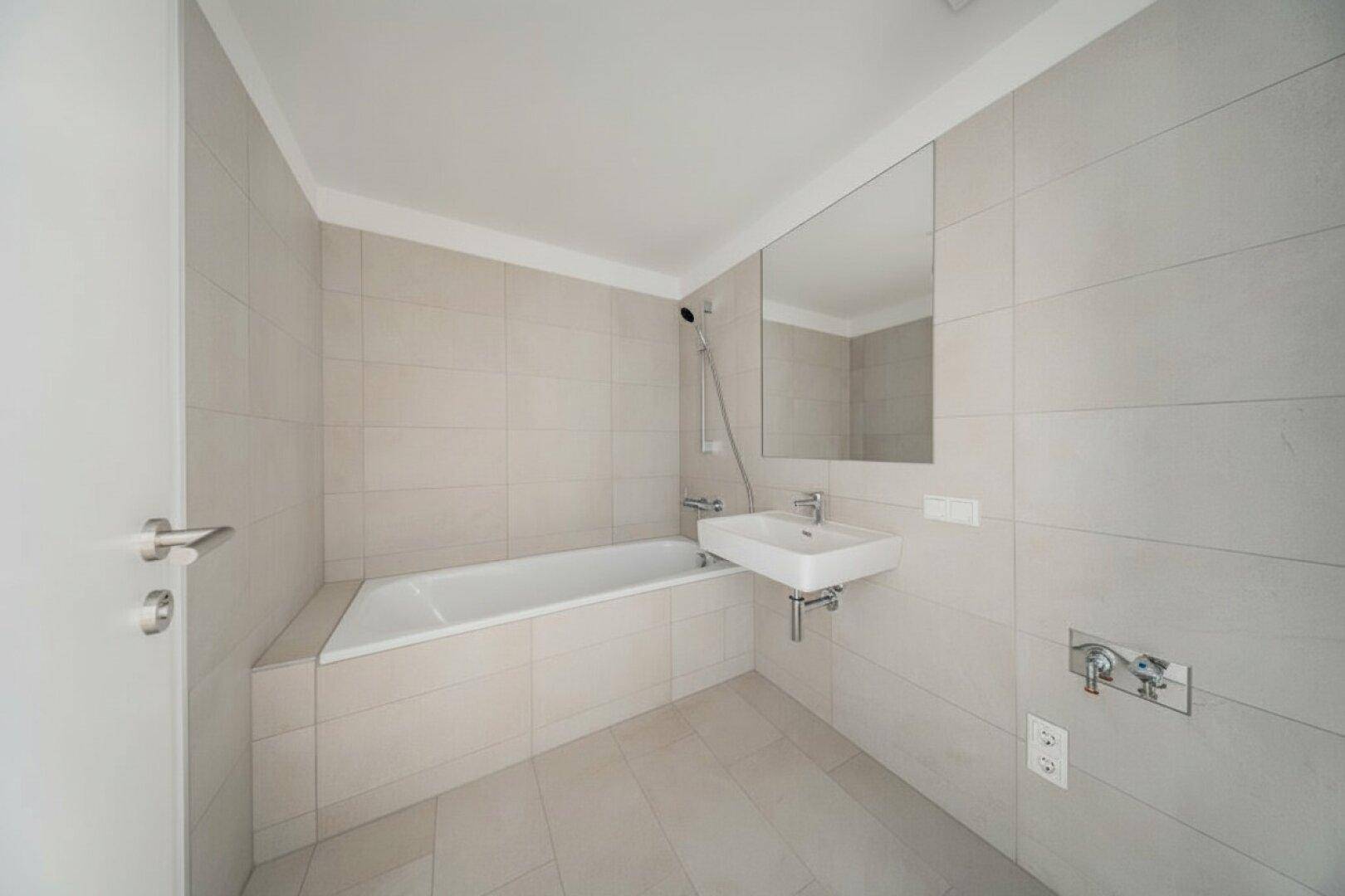 Modernes Badezimmer mit Badewanne, Waschbecken und hellen Fliesen, in gutem Zustand.