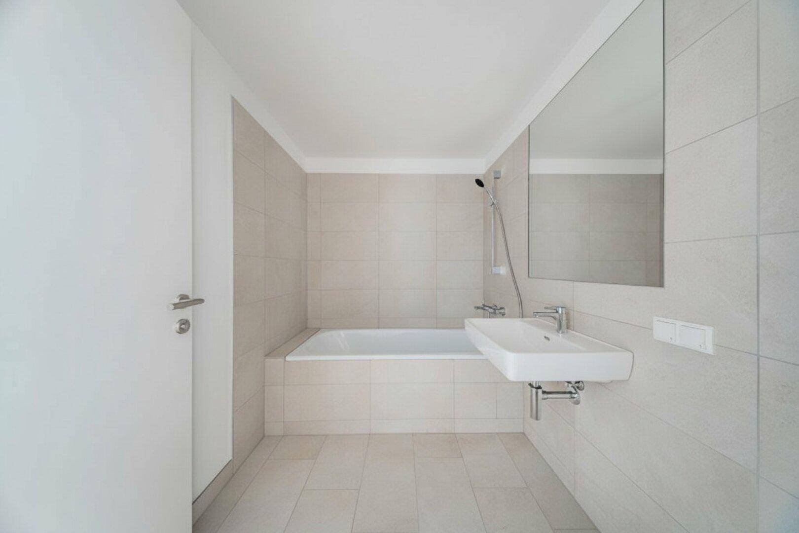 Helles Badezimmer mit Badewanne, Waschbecken und großem Spiegel, modern gefliest.