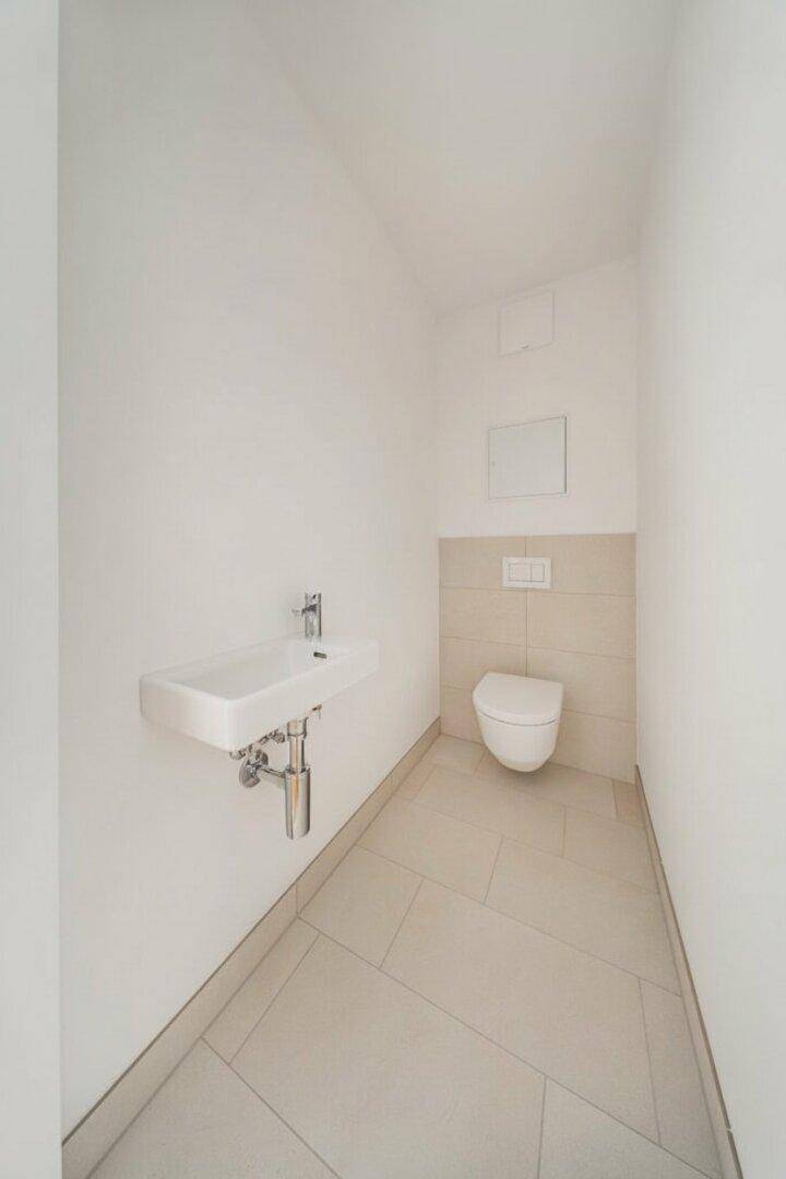 Separates Gäste-WC mit wandhängender Toilette und kleinem Waschbecken, hell gefliest.