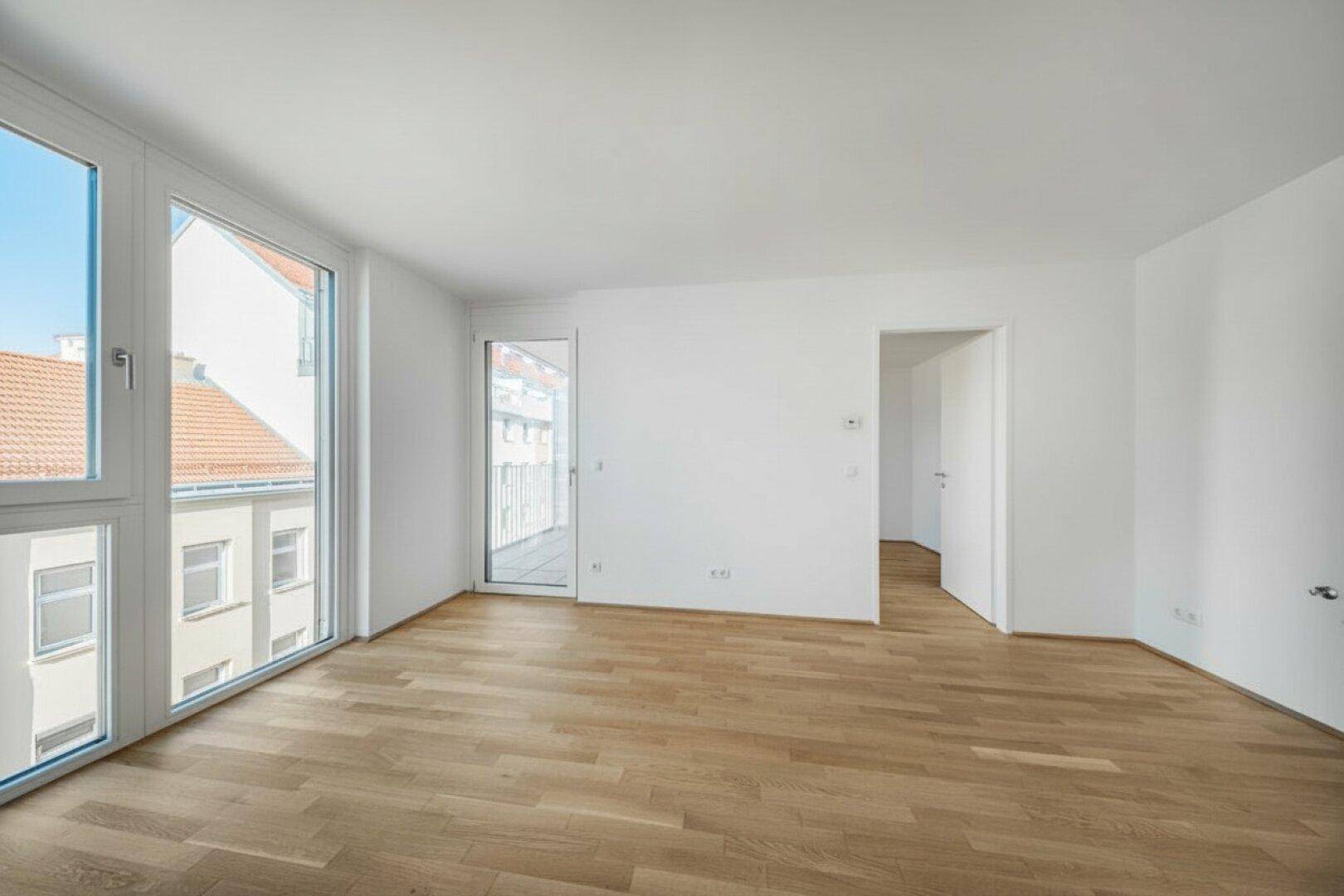 Heller, leerer Raum mit Holzboden und großen Fenstern, die viel Tageslicht hereinlassen.