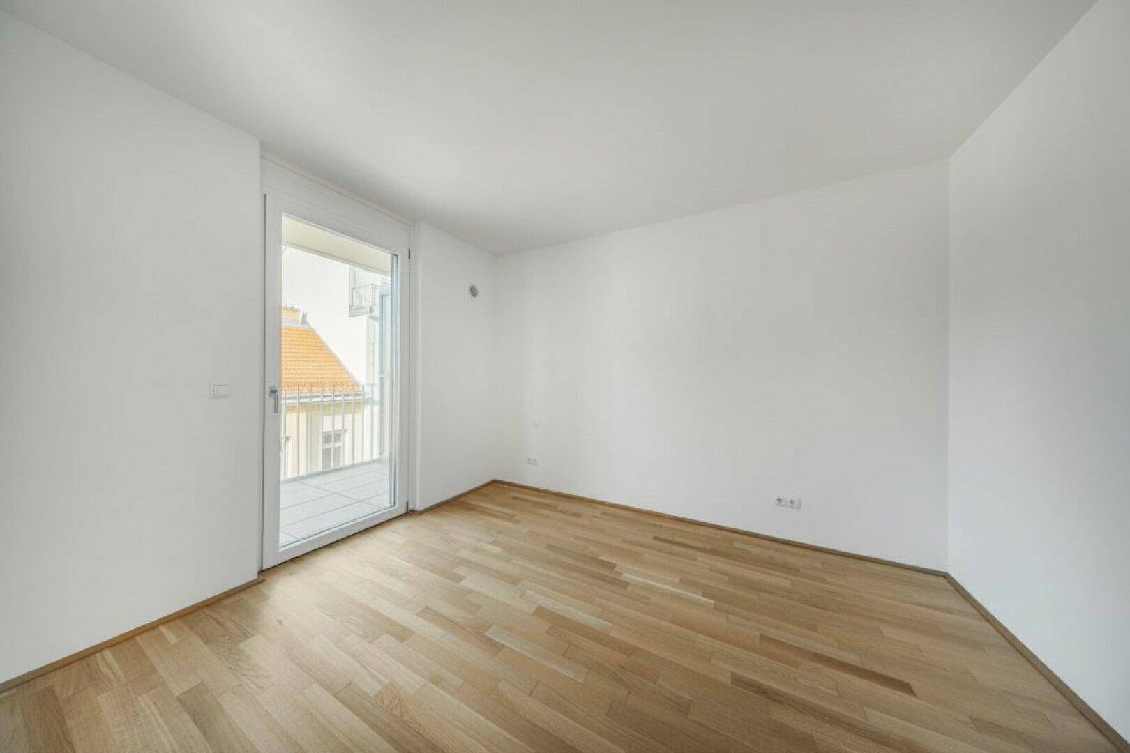 Helles, unmöbliertes Zimmer mit Holzboden und Balkonzugang, bereit zur individuellen Gestaltung.