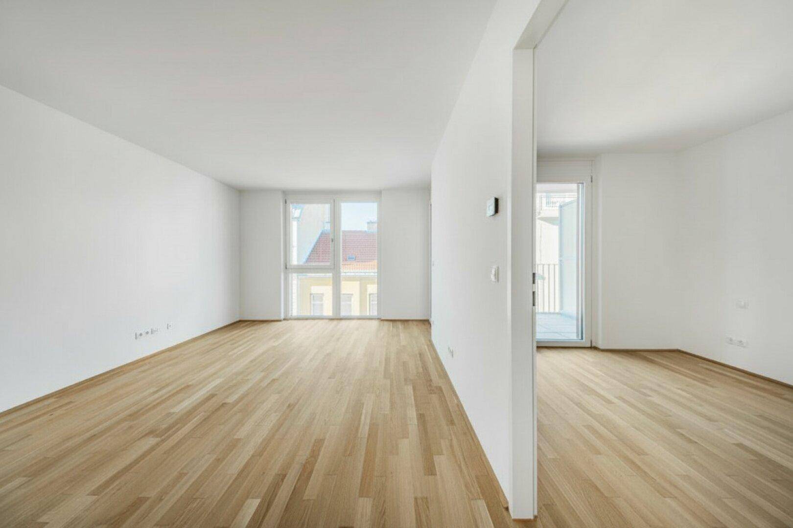 Großer, heller Raum mit Parkettboden und Fenstern, die viel Tageslicht hereinlassen.
